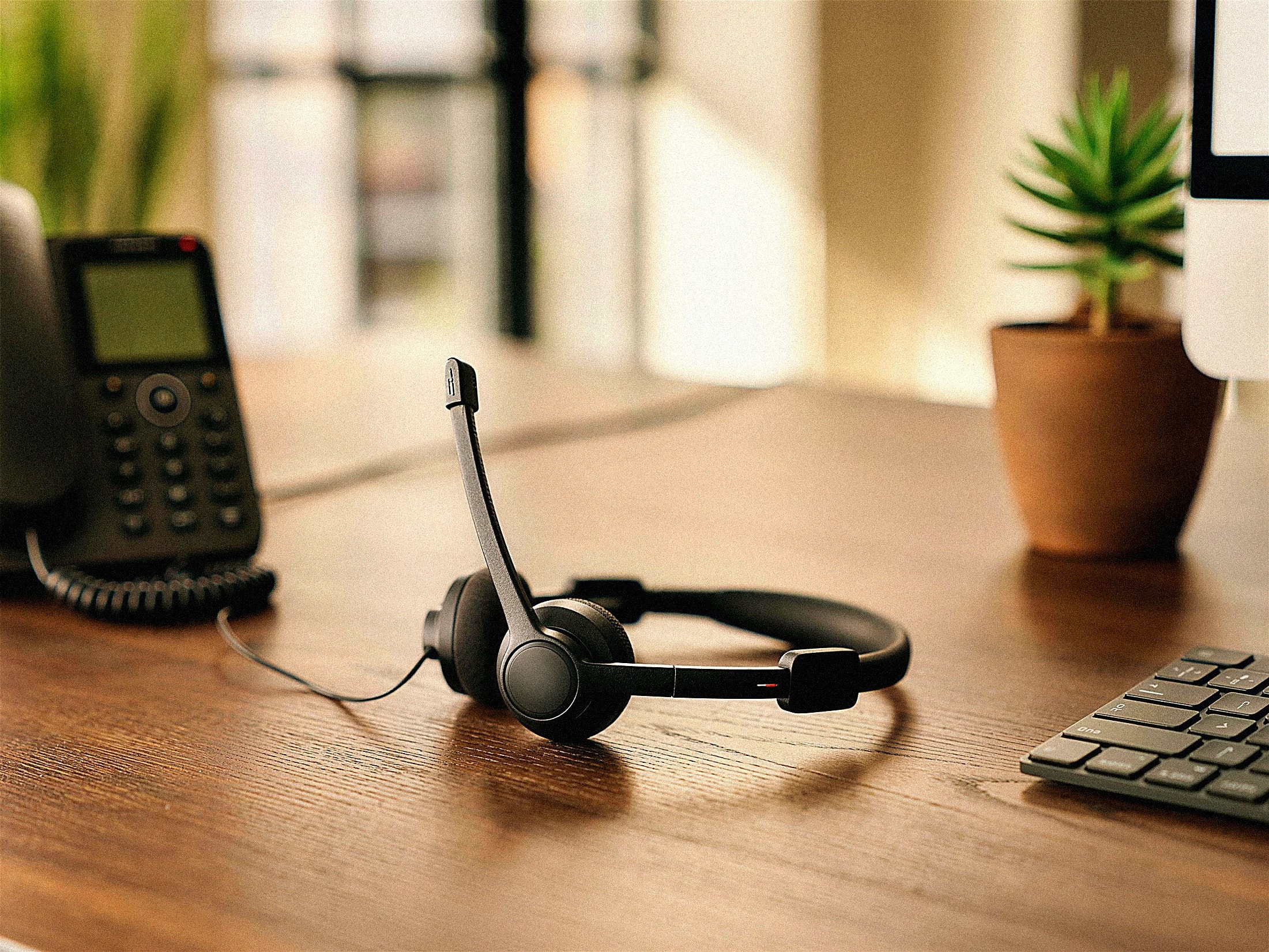 Telephone headset resting on a desk beside a desk phone in morning light
